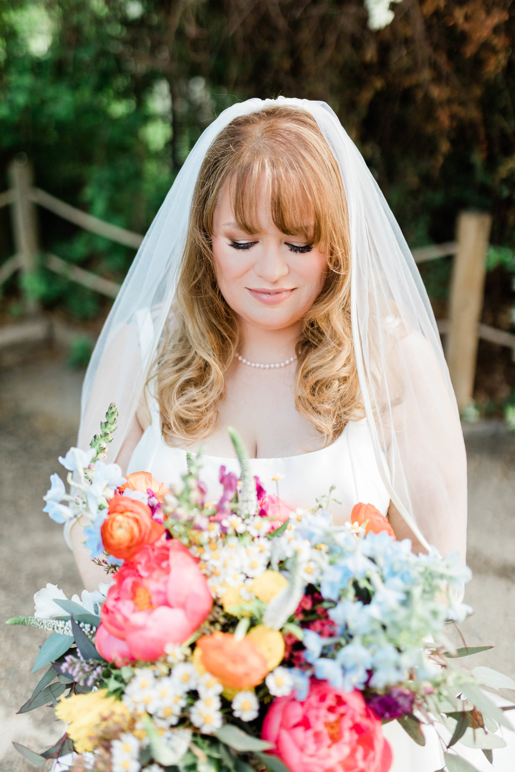 bride wearing veil and looking at colorful bridal bouquet