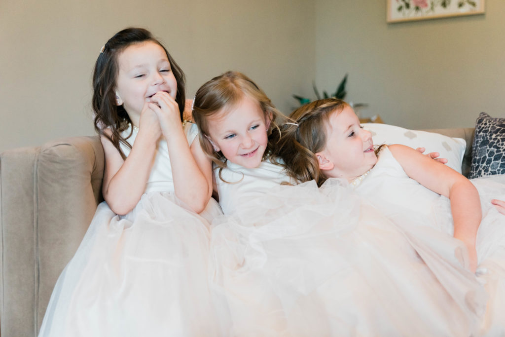 flower girls wearing ivory dresses smiling while bride gets dressed