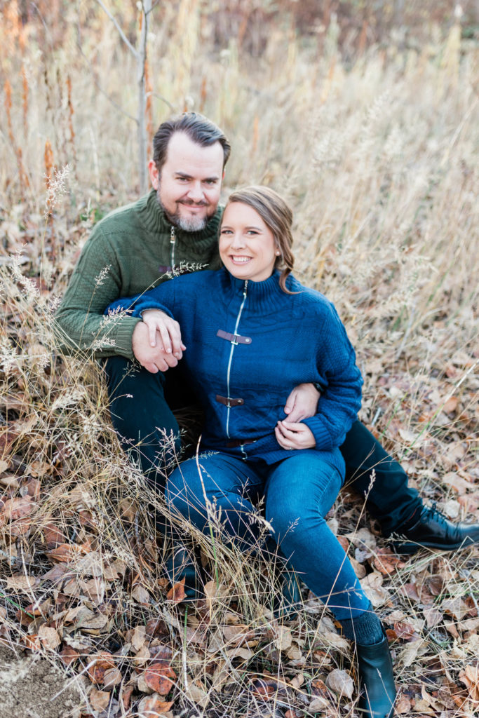 Boise wedding photographer captures man and woman sitting in grass wearing fall engagement outfits