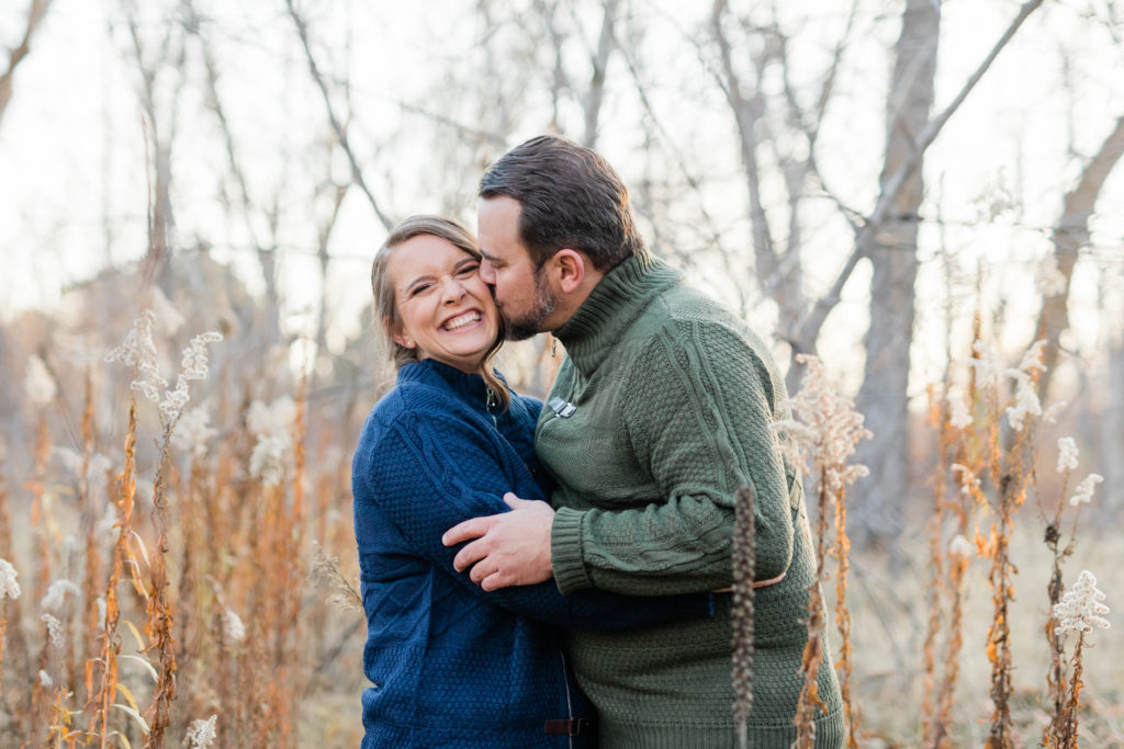 Boise wedding photographer captures man kissing woman's cheek wearing fall engagement outfits