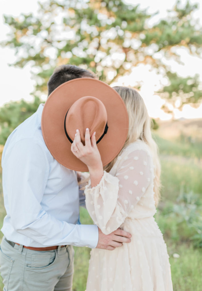 woman holding hat while she kisses fiance