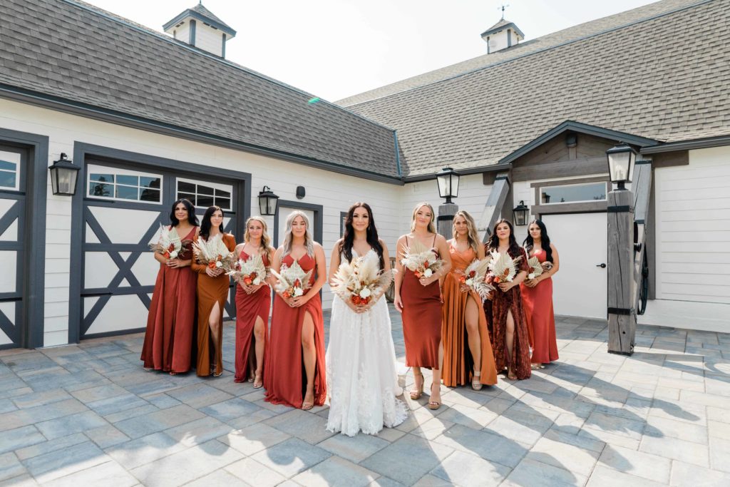 Boise wedding photographer captures bride standing with bridesmaids wearing various shades of rust dresses - boho mismatched bridesmaid dresses