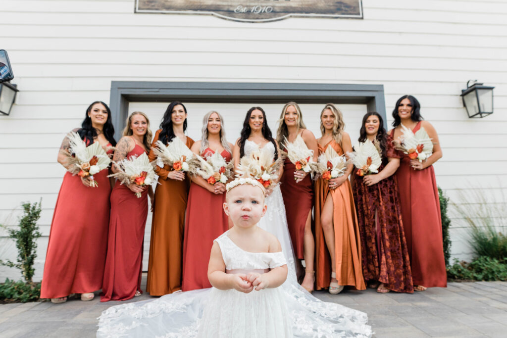 Boise wedding photographer captures bride standing with bridesmaids wearing mismatched gowns on Bohemian Inspired Mint Barrel Barn wedding day