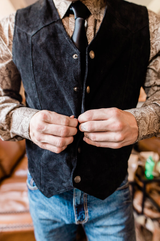 groom buttoning vest while getting ready for Mint Barrel Barn wedding